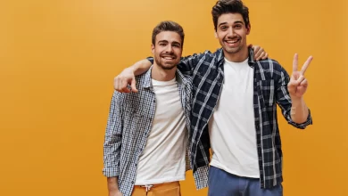 cheerful young men plaid blue shirts white t shirts colorful pants pose orange wall great mood smile 197531 23466