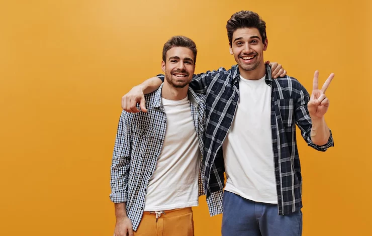 cheerful young men plaid blue shirts white t shirts colorful pants pose orange wall great mood smile 197531 23466