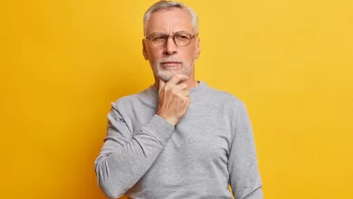 senior thougthful man holds chin looks pensively aside makes plannings wears spectacles casual grey jumper isolated vivid yellow wall 273609 44143